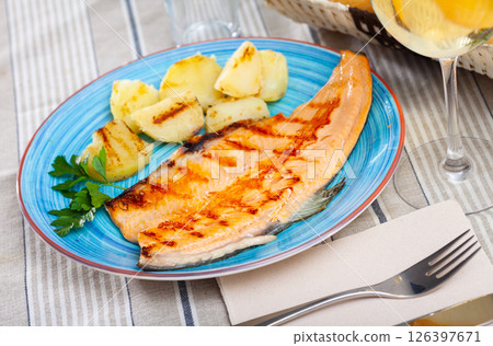 Fried trout fillet with baked potatoes on blue plate 126397671
