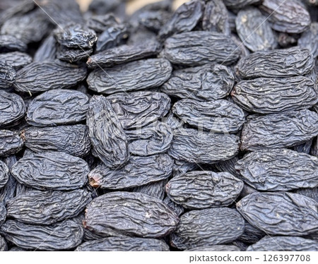 A close-up of a large mound of sun-dried black raisins laid out on a tray for sale at a farmer's market in Uzbekistan. A close-up of a large mound of sun-dried black raisins laid out on a tray for sale at a farmer's market in Uzbekistan. 126397708