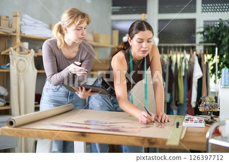 Dressmakers refining garment design with paper draft and tablet 126397712