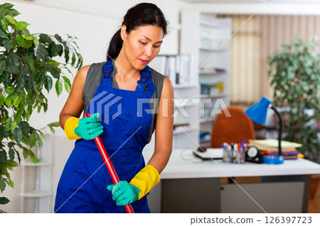 Female room cleaner sweeping floor in modern office 126397723