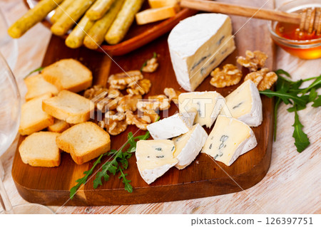 On table there is cutting board with blue cheese, honey, hardtack, walnut decorated with arugula 126397751