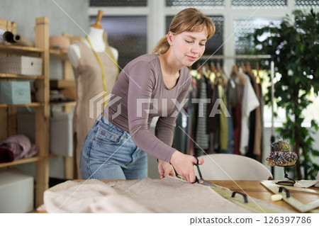 Female seamstress cutting fabric with scissors on worktable Female seamstress cutting fabric with scissors on worktable 126397786