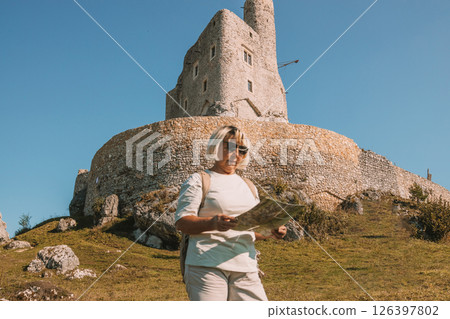 Happy old solo traveller senior woman in sunglasses with map near Mirow Castle, Poland at summer time. 126397802