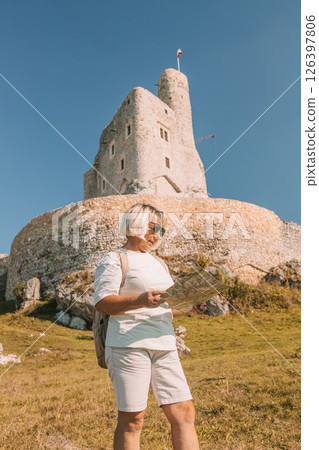 Happy old solo traveller senior woman in sunglasses with map near Mirow Castle, Poland at summer time. Happy old solo traveller senior woman in sunglasses with map near Mirow Castle, Poland at summer time. 126397806