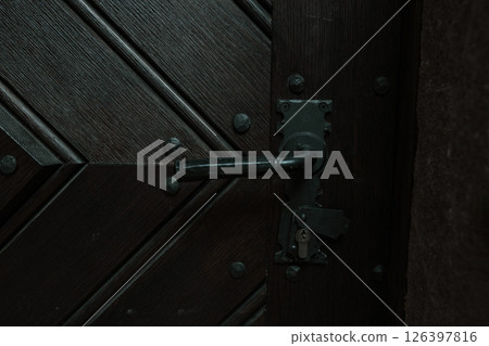 Close-Up of Vintage Wooden Door with Black Metal Handle and Diagonal Plank Design 126397816