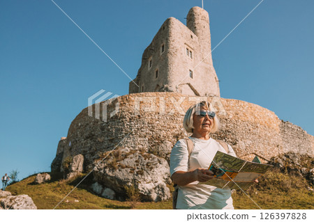 Happy old solo traveller senior woman in sunglasses with map near Mirow Castle, Poland at summer time. Happy old solo traveller senior woman in sunglasses with map near Mirow Castle, Poland at summer time. 126397828