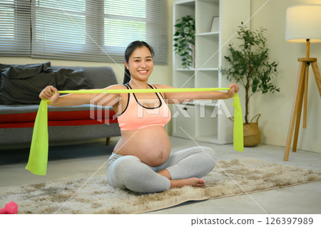 Smiling pregnant woman stretching exercises with resistance band at home 126397989