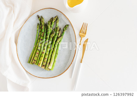 Grilled green asparagus on plate with hollandaise sauce on white table. Top view 126397992