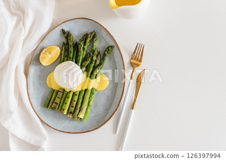 Poached egg with grilled asparagus and hollandaise sauce on white table. Top view Poached egg with grilled asparagus and hollandaise sauce on white table. Top view 126397994