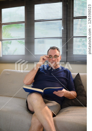 Relaxed older adult reading with concentration in a living room Relaxed older adult reading with concentration in a living room 126398023
