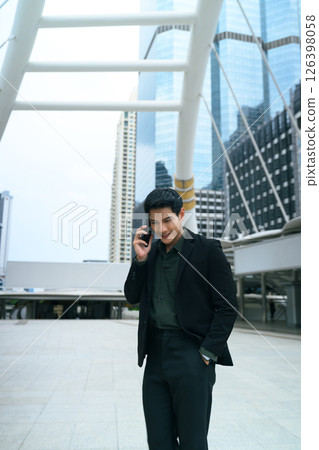 Smart businessman speaking on phone while walking through a modern cityscape Smart businessman speaking on phone while walking through a modern cityscape 126398058