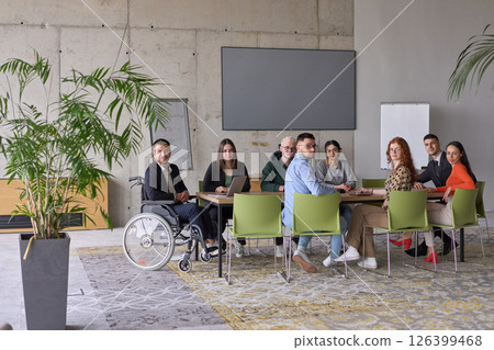 A diverse group of business professionals sitting in an office meeting with their director, who is in a wheelchair, fostering collaboration, leadership, and inclusivity A diverse group of business professionals sitting in an office meeting with their director, who is in a wheelchair, fostering collaboration, leadership, and inclusivity 126399468