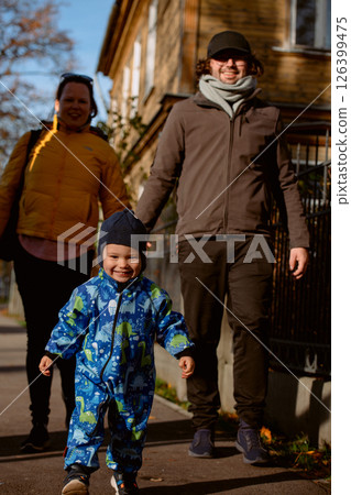 A loving couple strolls through a sunlit park with their young son, surrounded by the vibrant colors of autumn, enjoying a joyful and peaceful family moment together. 126399475