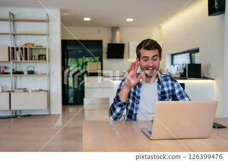 A freelancer sitting at a table in a modern living room, with headphones using a laptop for business video chat, conversation with friends and entertainment 126399476