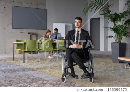 Business Director in a Suit Using a Wheelchair with Colleagues Conducting a Meeting Behind Him 126399573