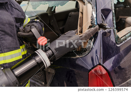 A dedicated team of professional firefighters employs specialized tools to cut and break through vehicle wreckage, showcasing their skilled collaboration and swift response in rescuing individuals 126399574
