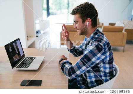 A freelancer sitting at a table in a modern living room, with headphones using a laptop for business video chat, conversation with friends and entertainment 126399586