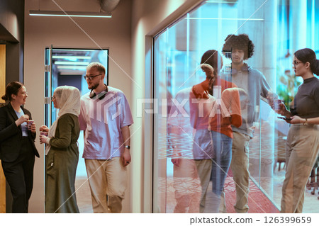 Amidst the modern glass walls of a startup office, a diverse group of colleagues, including an African American man, engage in a coffee-fueled discussion, exemplifying collaboration and innovation in 126399659