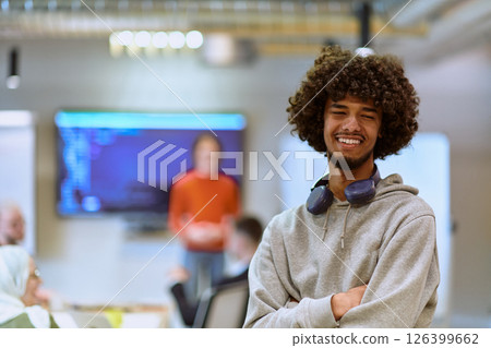 In a modern office environment, an African American young entrepreneur with headphones engages in work, while in the background, his dedicated colleagues exemplify teamwork and collaboration 126399662