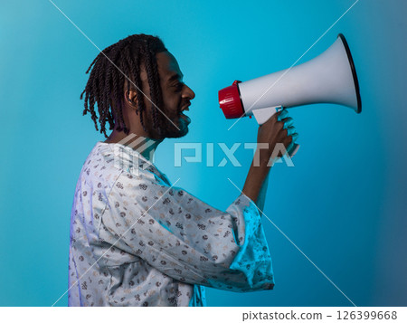 African American man dons traditional attire, passionately utilizing a megaphone against a striking blue background, symbolizing his vocal and cultural empowerment in the pursuit of social justice and 126399668