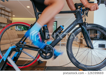 A triathlete riding a triathlon bike on a machine simulation in a modern living room. Training during pandemic conditions. 126399669