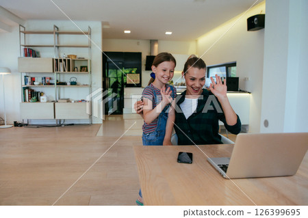 Mother with her daughter talking on laptop with family and friends while sitting in modern living room of big house. Mother with her daughter talking on laptop with family and friends while sitting in modern living room of big house. 126399695