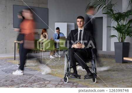 A businessman in a wheelchair navigating through a busy office, surrounded by his colleagues who are actively engaged in their work and collaboration 126399746