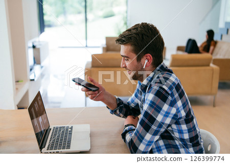 A freelancer sitting at a table in a modern living room, with headphones using a laptop for business video chat, conversation with friends and entertainment A freelancer sitting at a table in a modern living room, with headphones using a laptop for business video chat, conversation with friends and entertainment 126399774