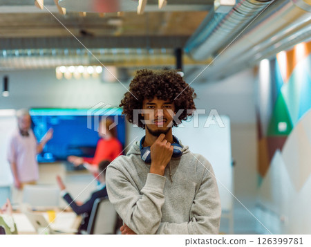 In a modern office environment, an African American young entrepreneur with headphones engages in work, while in the background, his dedicated colleagues exemplify teamwork and collaboration In a modern office environment, an African American young entrepreneur with headphones engages in work, while in the background, his dedicated colleagues exemplify teamwork and collaboration 126399781
