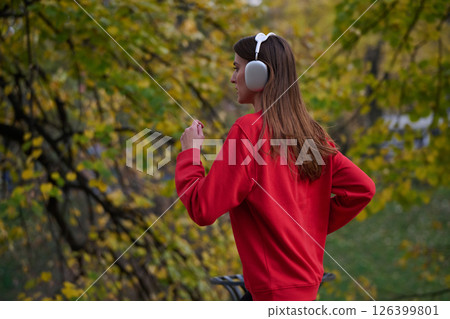 Young beautiful woman running in autumn park and listening to music with headphones on smartphone 126399801