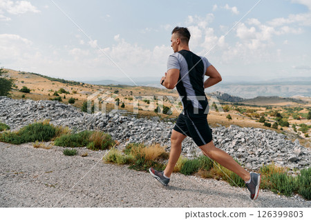 Determined Athlete Running Through Rugged Mountain Terrain at Sunrise. Determined Athlete Running Through Rugged Mountain Terrain at Sunrise. 126399803