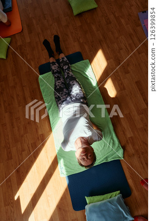 Senior woman practicing stretching and meditation on the floor, focusing on proper alignment and relaxation. 126399854