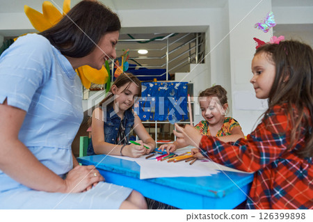 Creative kids during an art class in a daycare center or elementary school classroom drawing with female teacher. 126399898