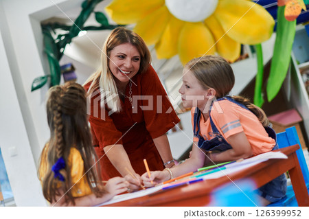 Creative kids during an art class in a daycare center or elementary school classroom drawing with female teacher. 126399952