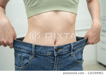 Young Asian woman losing weight wearing loose pants in oversize jeans. Young Asian woman losing weight wearing loose pants in oversize jeans. 126399961