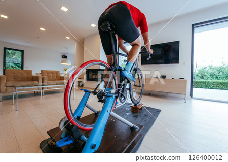 A triathlete riding a triathlon bike on a machine simulation in a modern living room A triathlete riding a triathlon bike on a machine simulation in a modern living room 126400012