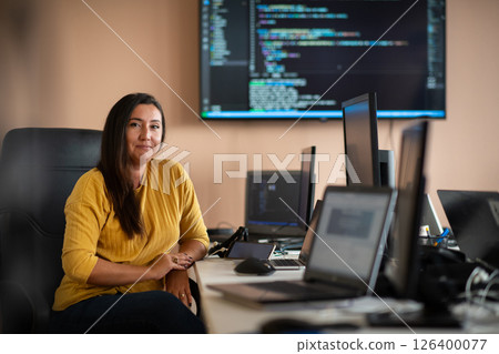 A businesswoman sitting in a programmer's office surrounded by computers, showing her expertise and dedication to technology. A businesswoman sitting in a programmer's office surrounded by computers, showing her expertise and dedication to technology. 126400077