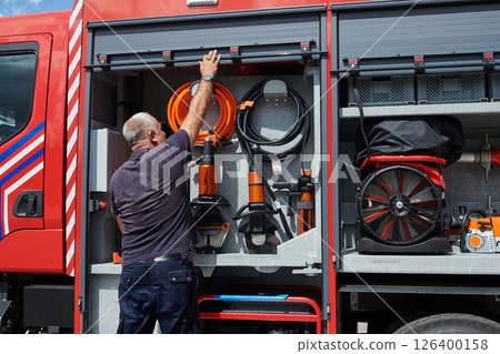 A dedicated firefighter preparing a modern firetruck for deployment to hazardous fire-stricken areas, demonstrating readiness and commitment to emergency response 126400158