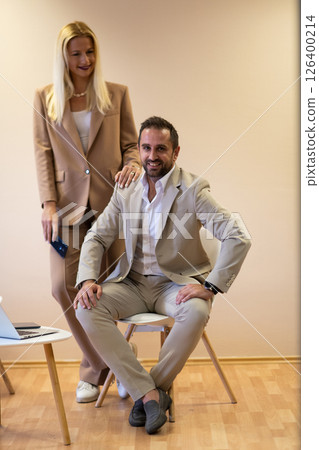 A business couple posing for a photograph together against a beige backdrop, capturing their professional partnership and creating a timeless image of unity and success. A business couple posing for a photograph together against a beige backdrop, capturing their professional partnership and creating a timeless image of unity and success. 126400214