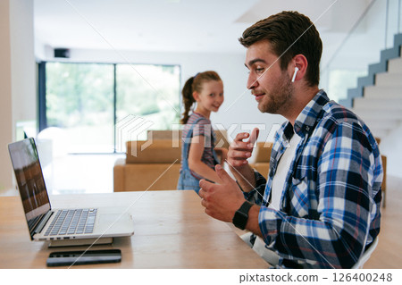 A freelancer sitting at a table in a modern living room, with headphones using a laptop for business video chat, conversation with friends and entertainment 126400248