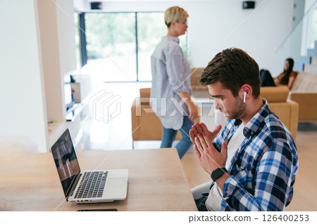 A freelancer sitting at a table in a modern living room, with headphones using a laptop for business video chat, conversation with friends and entertainment 126400253