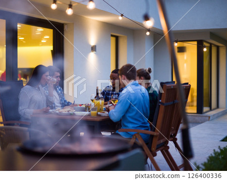 A group of young diverse people having dinner on the terrace of a modern house in the evening. Fun for friends and family. Celebration of holidays, weddings with barbecue 126400336