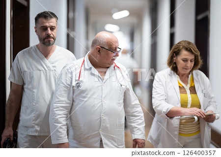 A group of healthcare professionals in white uniforms walking through a hospital hallway while reviewing patient documents and discussing treatment plans. 126400357