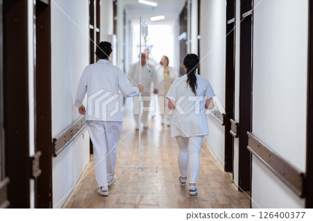 Medical personnel, including doctors and nurses, urgently respond in a busy hospital hallway, showcasing their quick action and teamwork in a critical situation 126400377