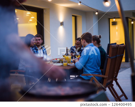 A group of young diverse people having dinner on the terrace of a modern house in the evening. Fun for friends and family. Celebration of holidays, weddings with barbecue A group of young diverse people having dinner on the terrace of a modern house in the evening. Fun for friends and family. Celebration of holidays, weddings with barbecue 126400495