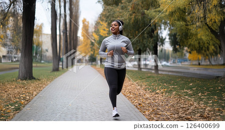 Tired African woman running outdoors in a city park on a crisp autumn morning with headphones on. Generated image 126400699