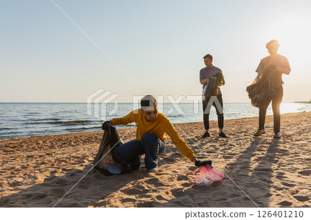 Earth day. Volunteers activists team collects garbage cleaning of beach coastal zone. Woman mans puts plastic trash in garbage bag on ocean shore. Environmental conservation coastal zone cleaning 126401210