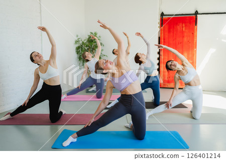 Yoga class Pilates workout. Group of sporty people doing exercise in studio class for yoga wellness mindfulness meditation. Personal trainer men women practicing yoga in gym training stretching indoor Yoga class Pilates workout. Group of sporty people doing exercise in studio class for yoga wellness mindfulness meditation. Personal trainer men women practicing yoga in gym training stretching indoor 126401214
