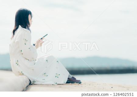 A woman in a floral dress looking at her smartphone on the beach 126402551