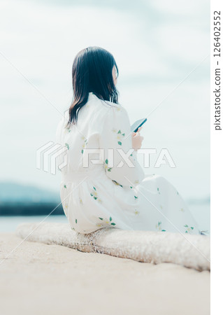 A woman in a floral dress looking at her smartphone on the beach 126402552